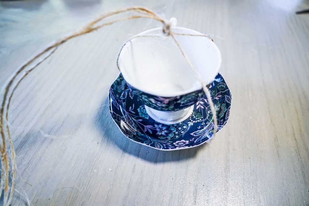 person tying twine to hang a teacup bird feeder